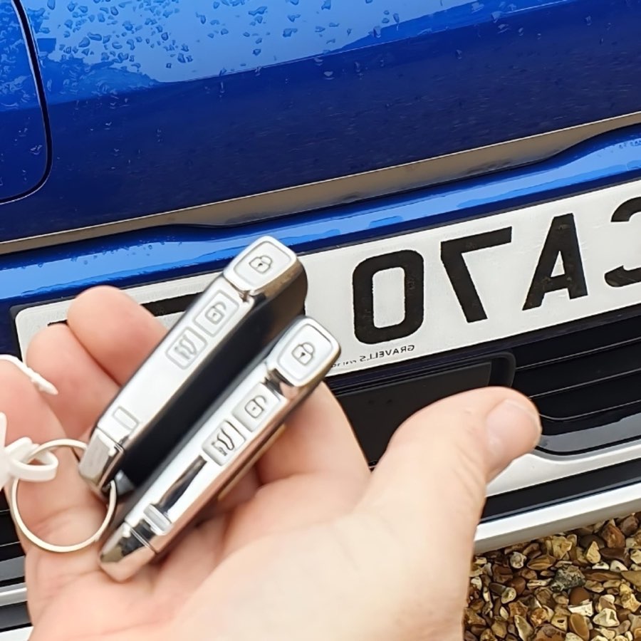 Two replacement car key fobs held in front of a car